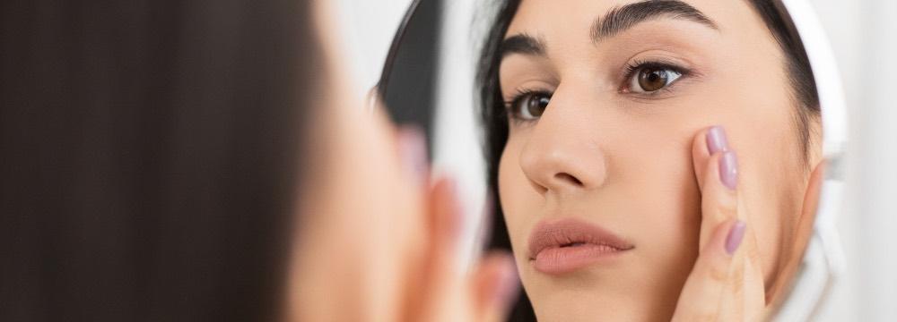 woman inspecting facial fullness in the mirror