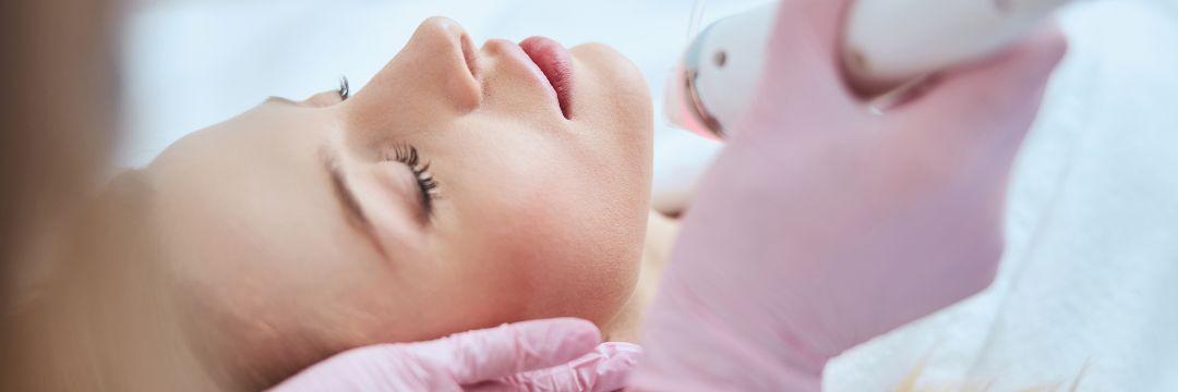 Woman receiving microneedling treatment from an aesthetician with pink gloves 